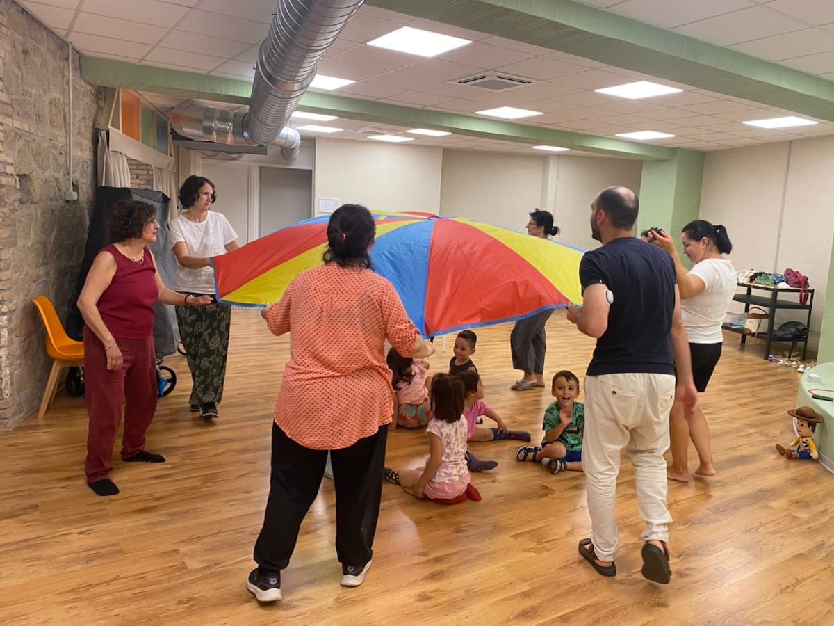Adulti e bambini tengono un grande telo colorato al centro di una sala