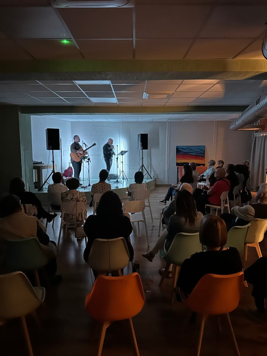 Due musicisti sul palco, con la chitarra, davanti al pubblico seduto